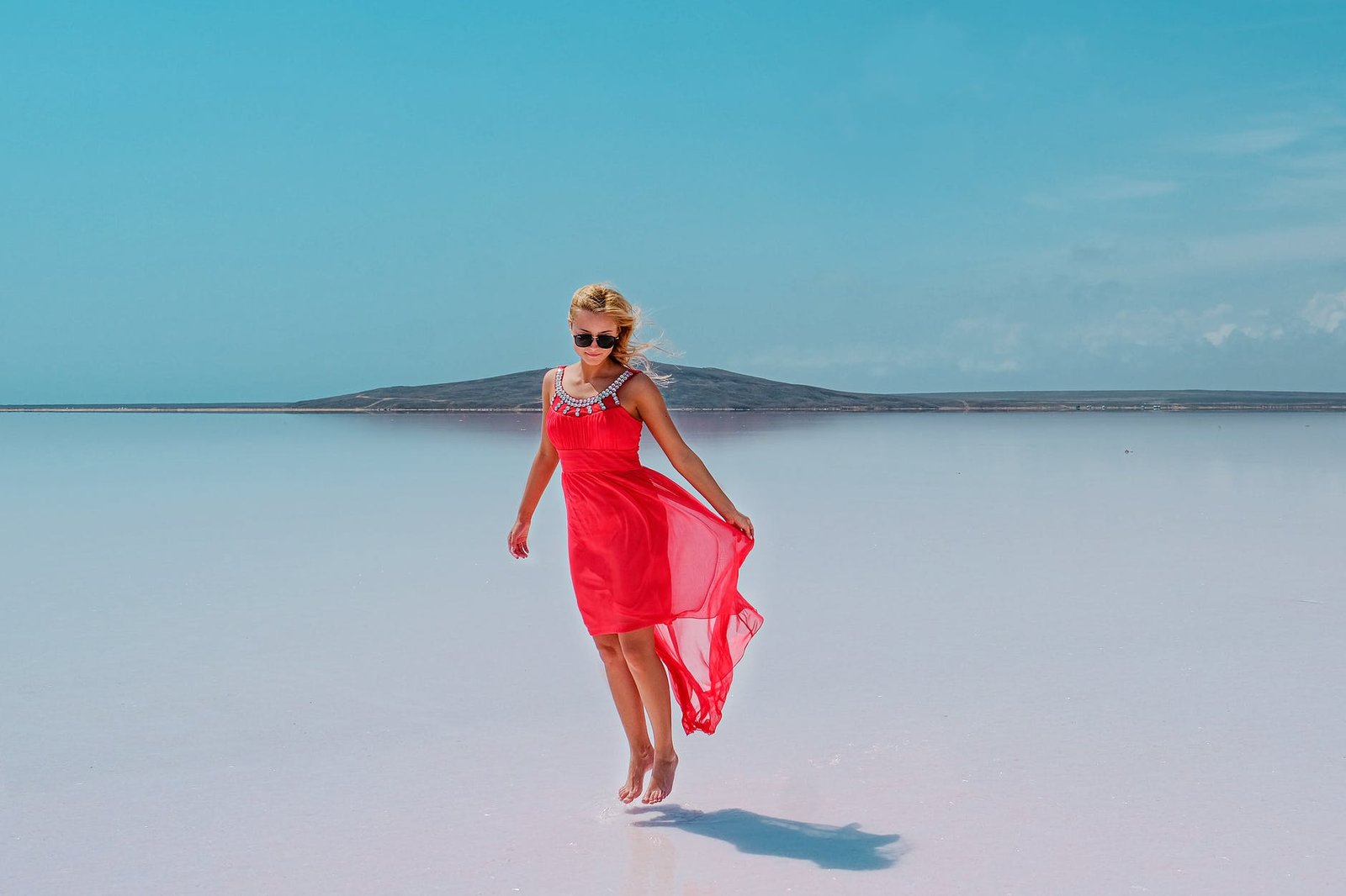 woman in sunglasses jumping over wet sand